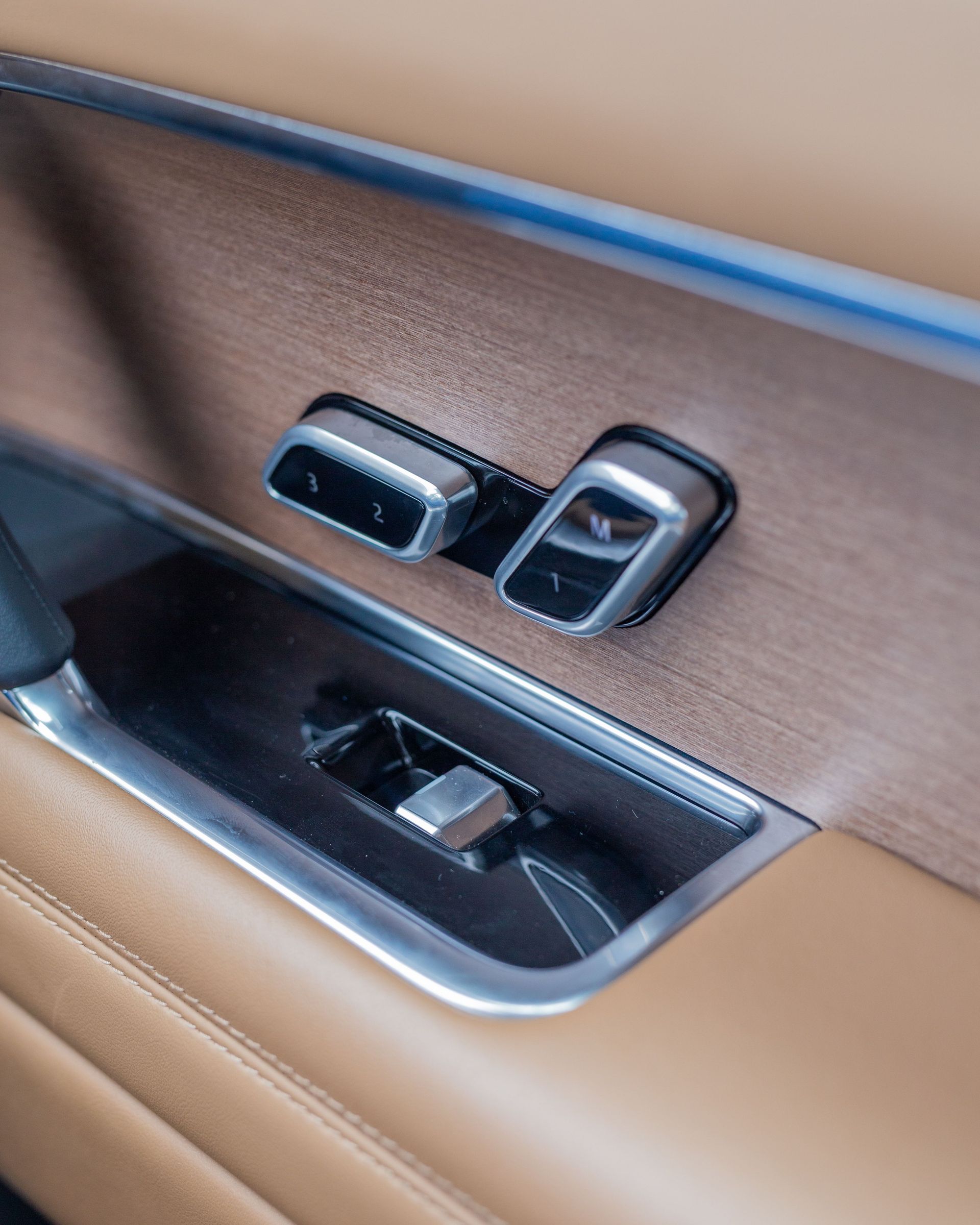 Close-up of luxury SUV's door panel featuring seat adjustment controls in elegant brown and chrome.
