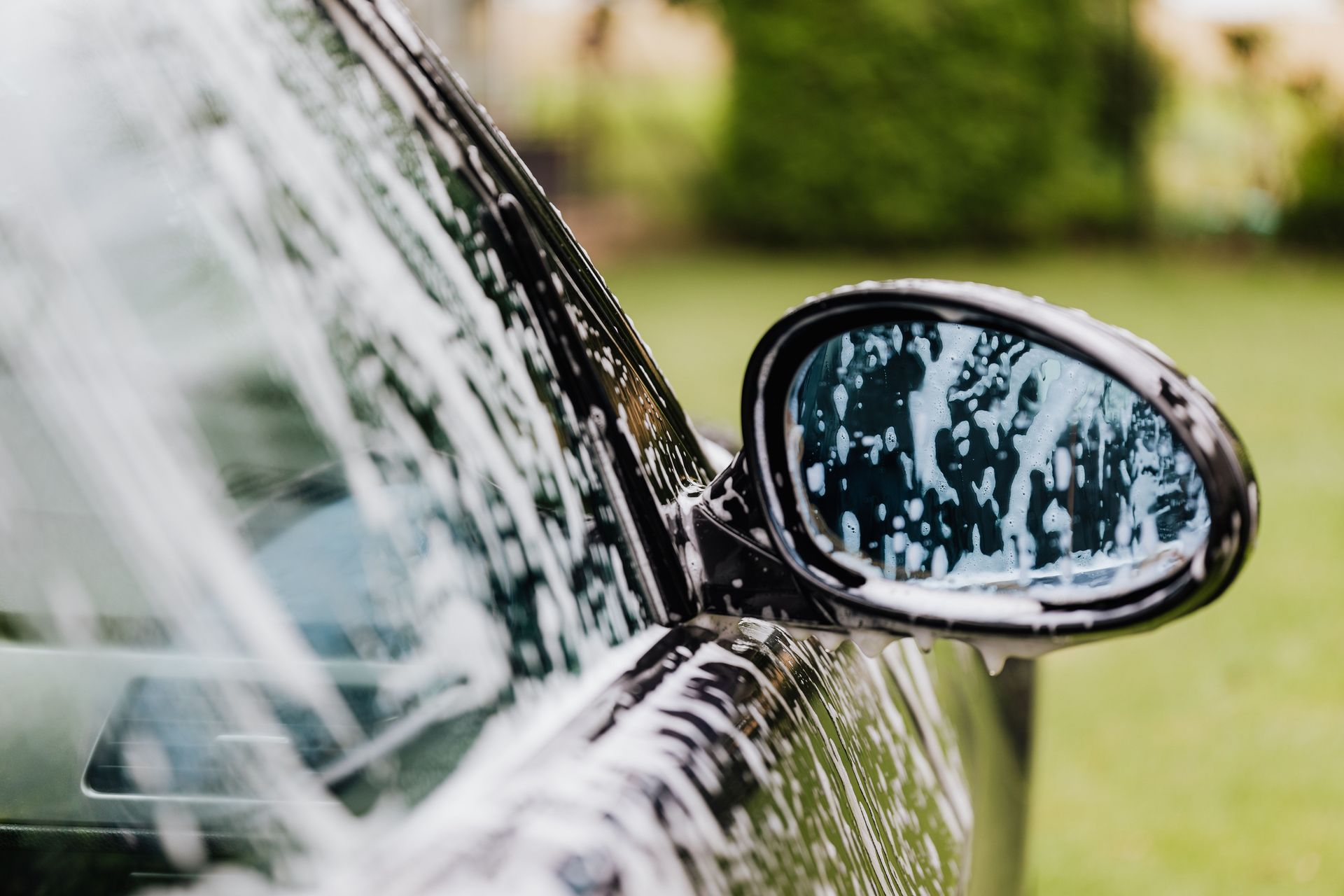 A detailed view of a car side mirror with soap suds, highlighting car wash detail.